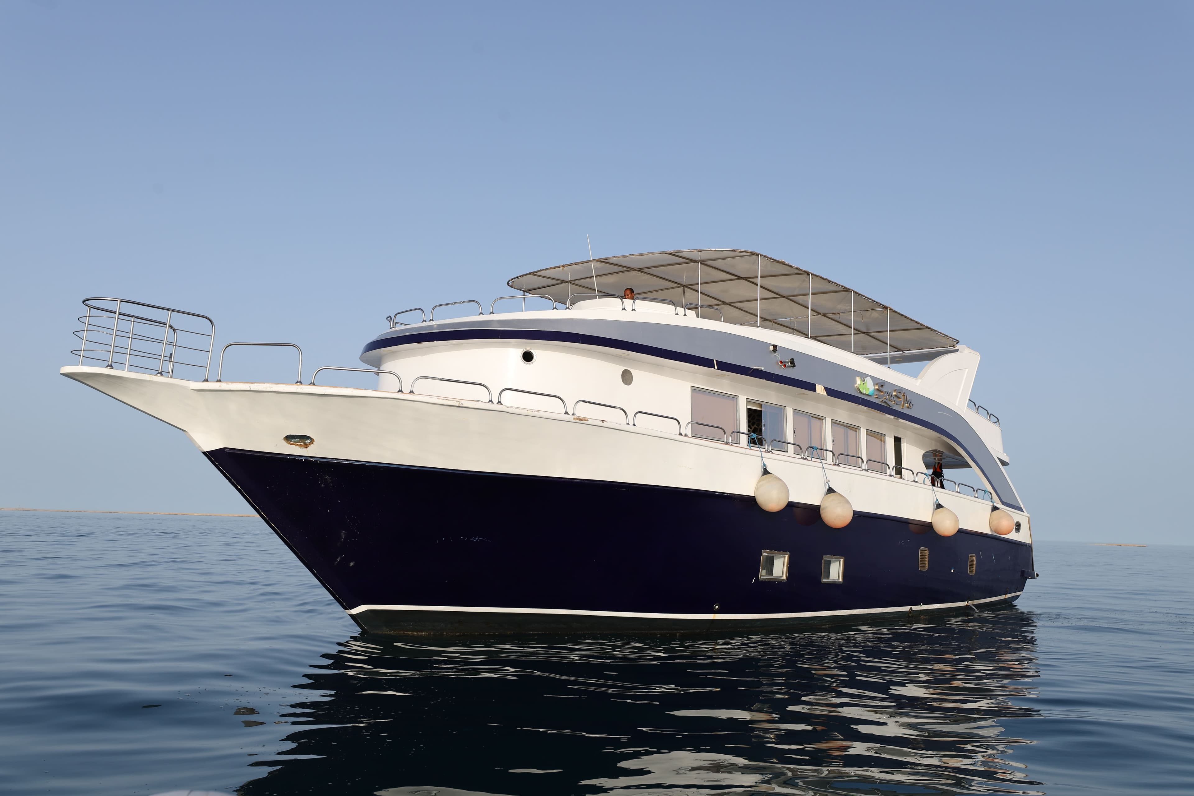 Navy and white yacht at anchor on a glassy sea under a shaded sun deck